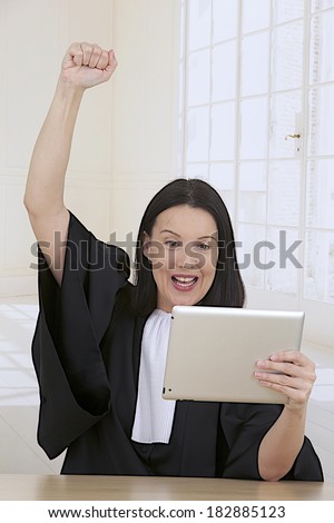 woman lawyer attorney wearing classic French  black white  gown holding digital tablet ,hands fists raised up cheering success