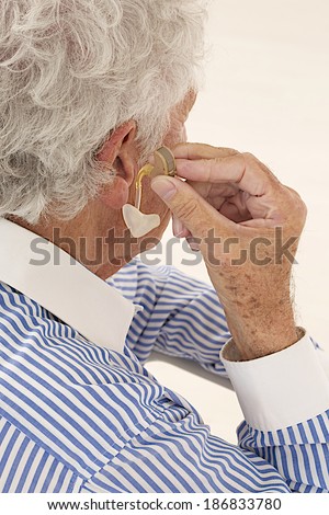 Closeup of a senior  man inserting a hearing aid in her hear. Focus on the hearing aid.