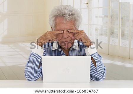 Senior businessman in front of laptop rub eyes