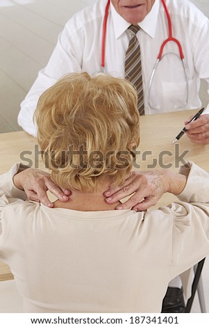 Mature woman holding her neck and talking with senior male  doctor.