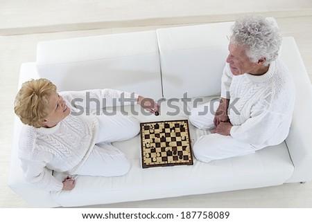 Top view of a senior couple sitting on floor playing chess at home on the couch