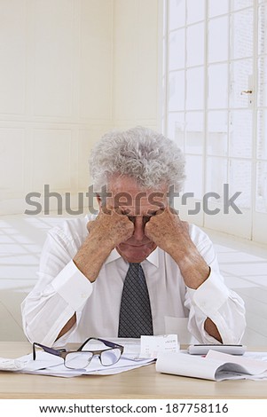Senior nan at desk in shirt and tie looking depressed, holding his head and worrying about money and bills