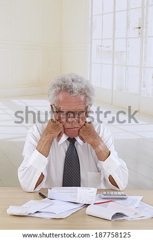 Senior man  at desk in shirt and tie holding his head and worrying about money.