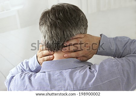 back view of a businessman sitting in a desk with pain in his neck,