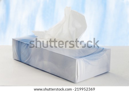 A hand pulls a tissue from a tissue box.