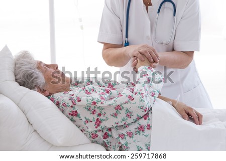 medical doctor holding senior patient\'s hands and comforting her
