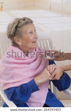 Caregiver giving glass of water to an elegant senior woman at nursing home