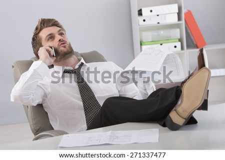 Young businessman in office sitting with feet on desk talking on cellphone.
