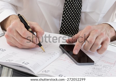 Image of  business man\' s hands planning on agenda book, and smart phone  in office