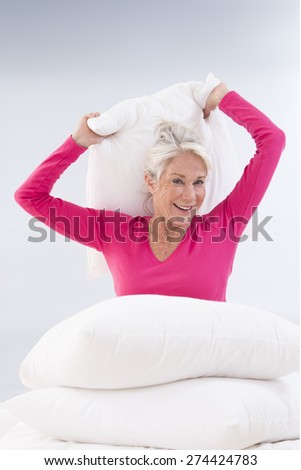 Attractive senior woman in bed having a pillow fight