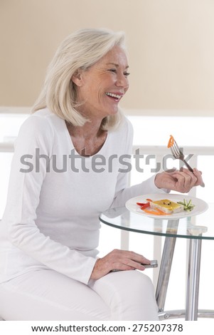 Senior woman eating a healthy salad at the kitchen