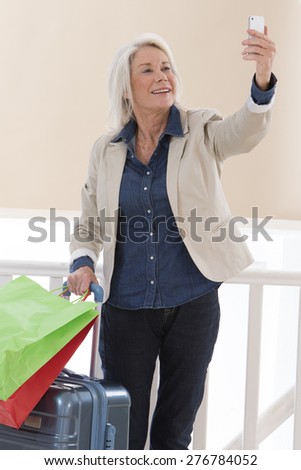 happy  senior woman picturing herself with  smart phone smiling while holding her luggages and shopping bags