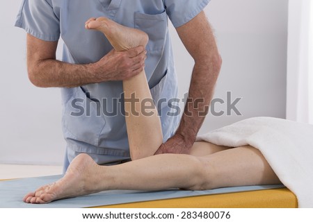 Physiotherapist stretching his patients leg in medical office
