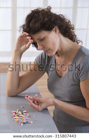 sick  woman with a lot of pills lying on the table and holding one  pills in her hand