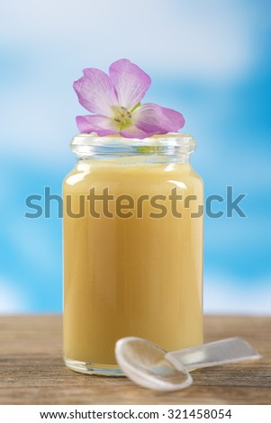 raw organic royal jelly in a small bottle with flowers