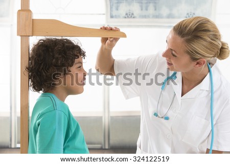 Doctor measures growth smiling boy in medical office, profile vi