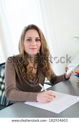 young female student doing homework with computer and cell phone
