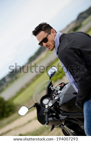 handsome young biker man riding a black motorbike with sunglasses