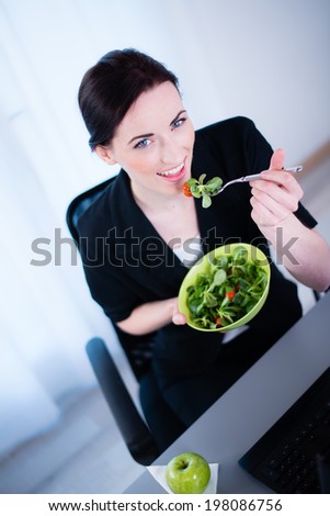 cheerful young caucasian business woman enjoying fresh salad for lunch break at office desk