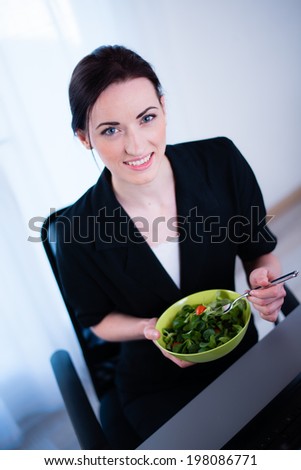 cheerful young caucasian business woman enjoying fresh salad for lunch break at office desk