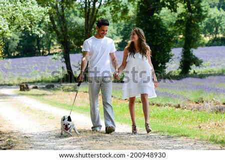 young happy man and woman couple walking with their dog in summer vacation in countryside