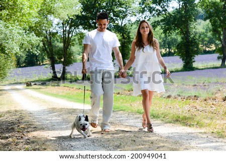 young happy man and woman couple walking with their dog in summer vacation in countryside
