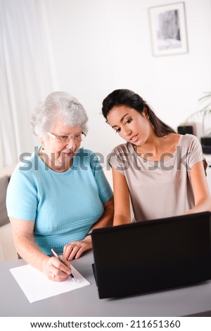 cheerful young woman helping an elderly person using laptop  computer for internet search and email