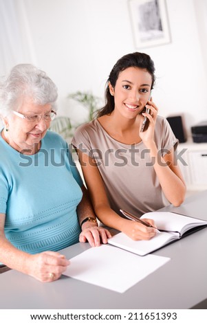 cheerful young woman helping an old person doing paperwork and telephone call