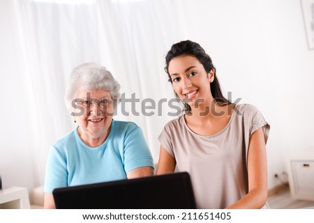 cheerful young woman teaching computer and internet to an elderly person