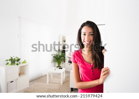 cheerful young woman opening her house front door and inviting friends at home