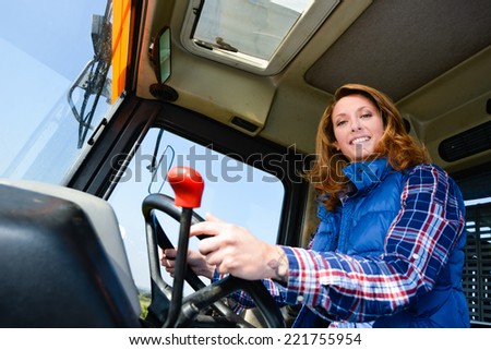 cheerful young woman farmer driving tractor in the fields during harvest in countryside