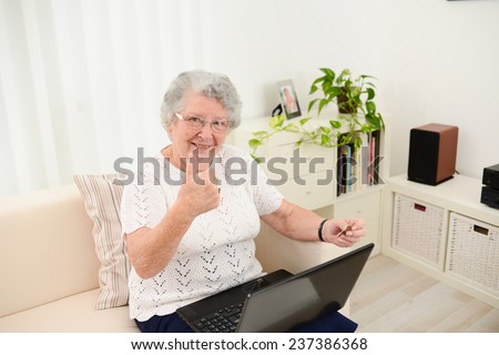 cheerful elderly woman web surfing and shopping on internet at home with laptop