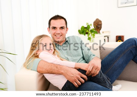 happy handsome young daddy and his young daughter lying down on sofa at home