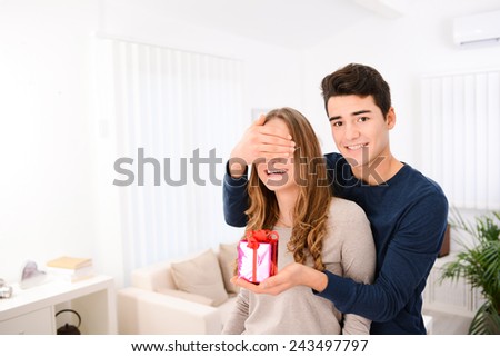 cheerful young couple man and woman at home offering to each other gifts for lover\'s valentine day