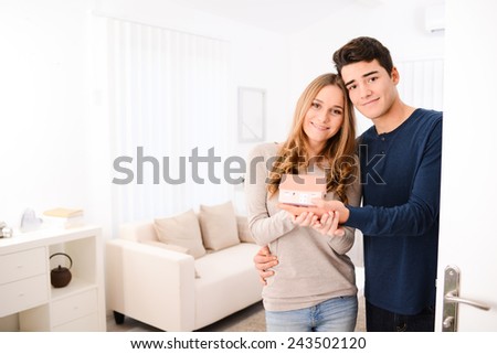 happy young couple showing reduced model of their new house at their open door