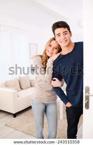 happy young couple welcoming friends at their apartment open door