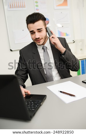 young businessman in office working on laptop computer and phone