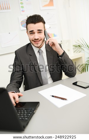 young businessman in office working on laptop computer and phone