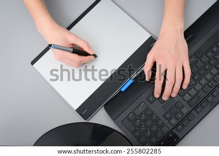 close up detail of hands working with graphic tablet and a desktop keyboard