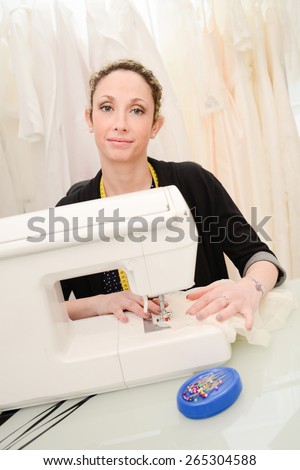 cheerful young seamstress sewing a wedding dress on her sewing machine