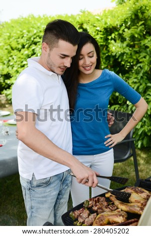 cheerful young couple cooking barbecue outdoor in summer garden party