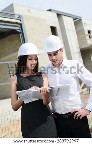 foreman architect man and woman supervising building construction site with blueprint