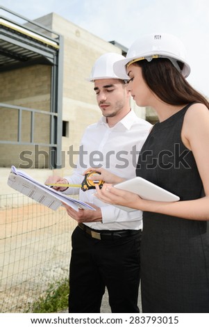 foreman architect man and woman supervising building construction site with blueprint