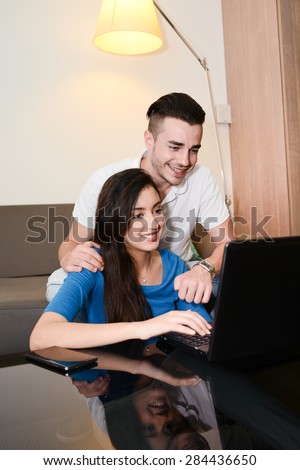 cheerful happy young couple at home web surfing and playing together with computer tablet