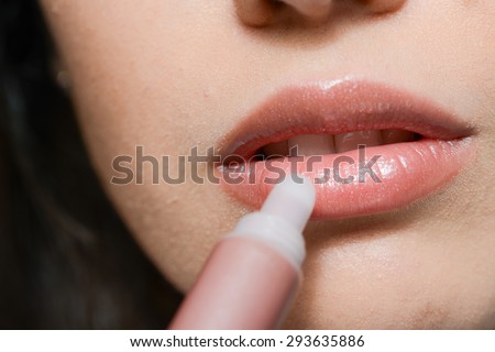 mouth close-up of a beautiful young woman putting on her lipstick gloss