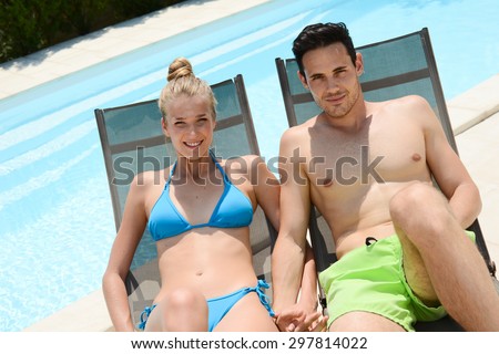 beautiful young couple in swimsuit relaxed in deck chairs by the pool