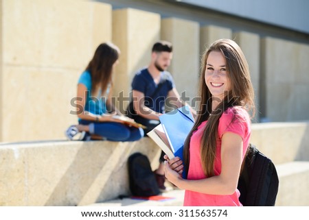 portrait of an attractive cheerful young student woman outdoor in front of high school campus