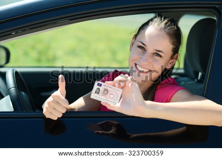 cheerful and happy young woman in her car showing her new driving license