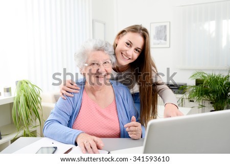 young woman helping an old senior woman doing paperwork and administrative procedures with laptop computer at home