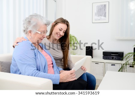 cheerful young girl sharing time with an old senior woman and teaching internet with computer tablet